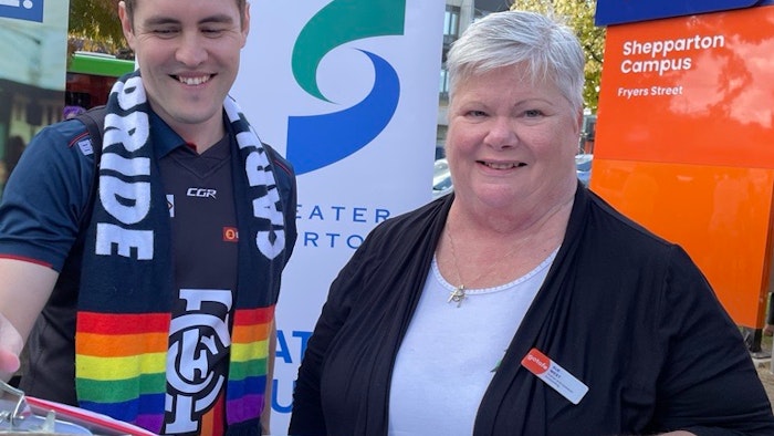 Daniel wearing a pride scarf, looking down and smiling next to Sue who is smiling at the camera