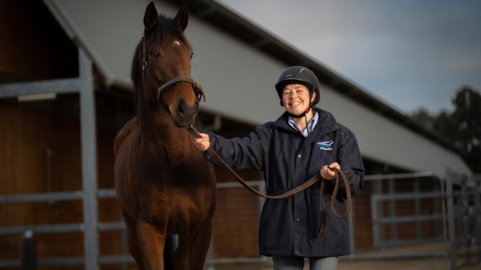 Equine trainer leading horse and smiling