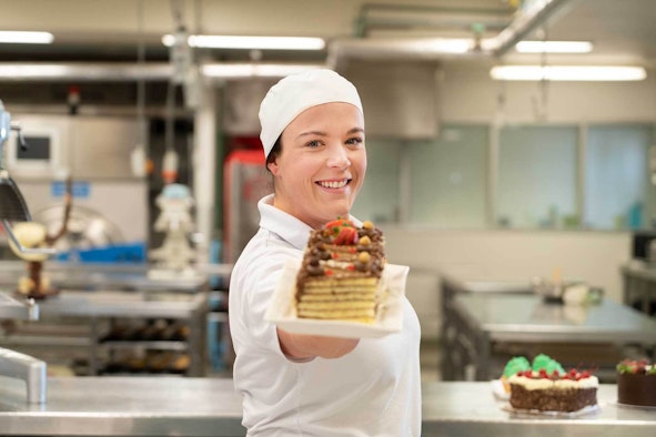 Baking student holding out cake on plate to camera