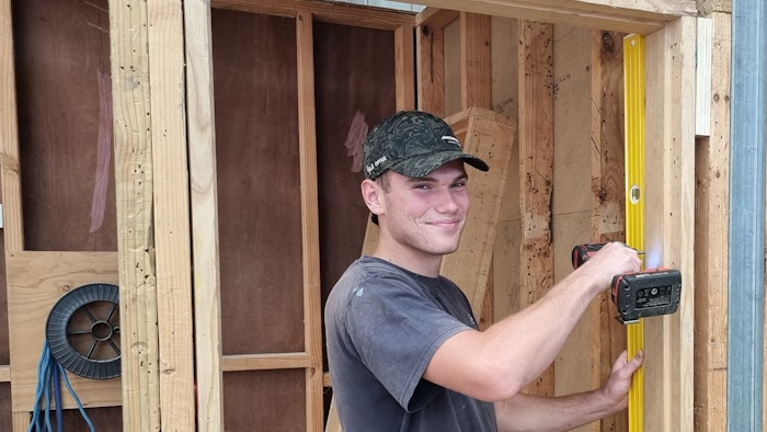 Man wearing cap standing and holding a drill next to wooden planks