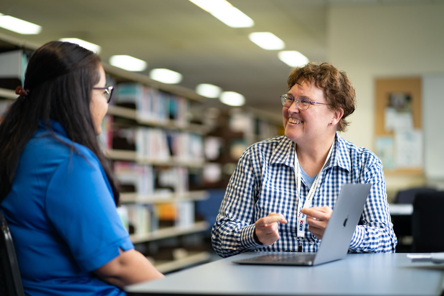 A student and staff member sitting at a table talking with a laptop