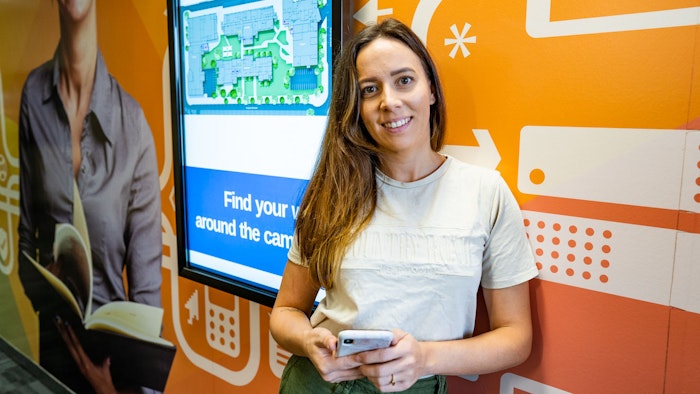 Student standing against a wall holding a phone